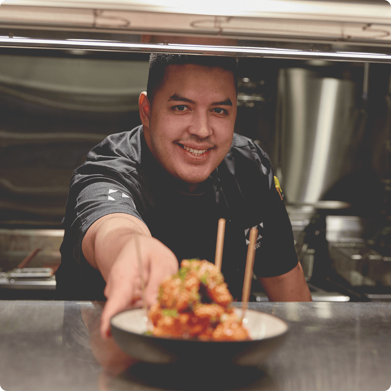 A chef serving a dish across the kitchen pass over.