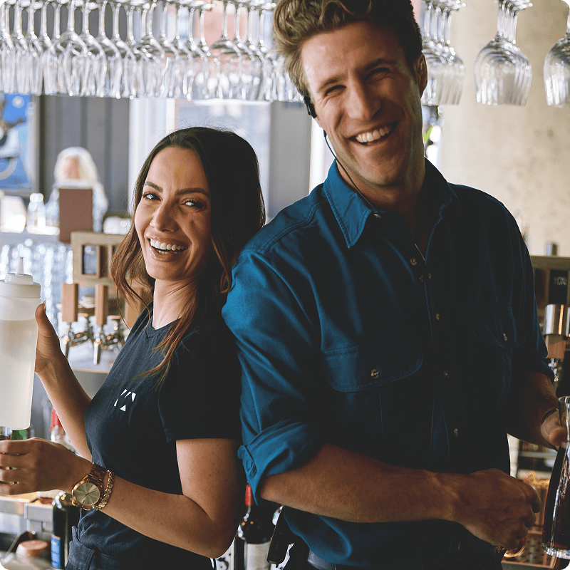 A male and female bartender standing next to each other smiling. 
