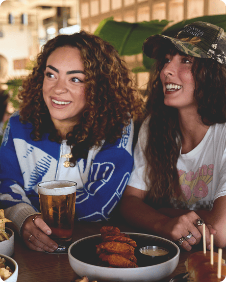 Two women enjoying a beer and chicken wings at King Taps