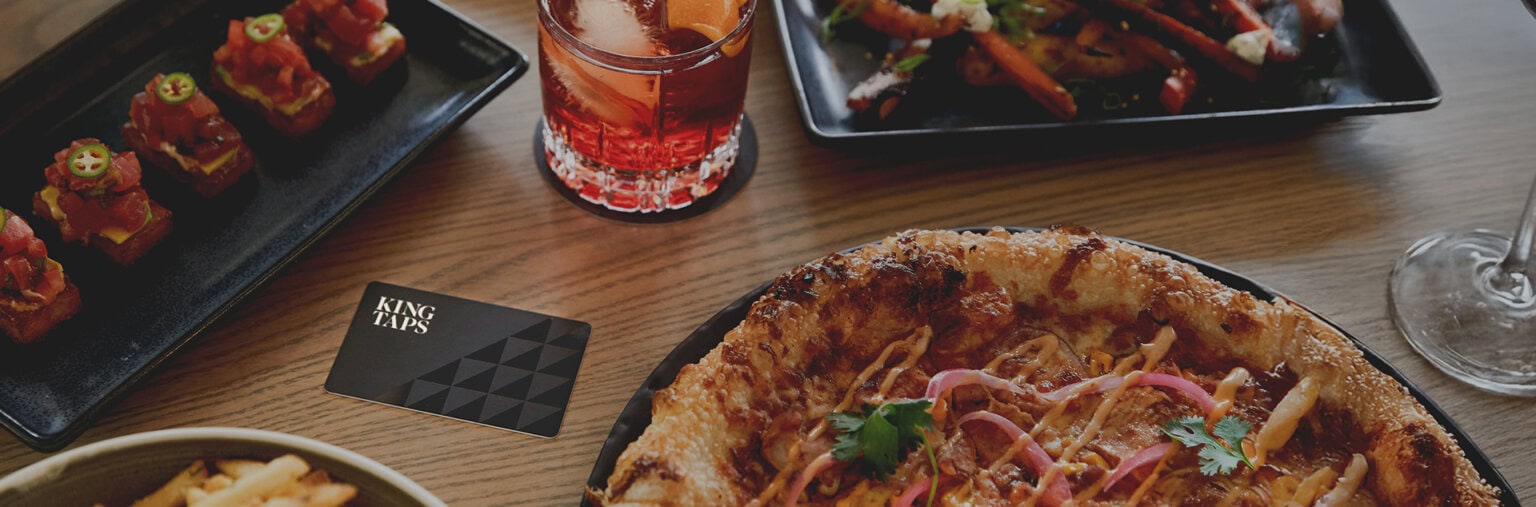 Table spread with pizza, a cocktail, sushi bite and a King Taps branded gift card