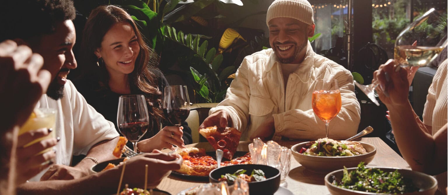 Group of people enjoying a meal together with drinks and shared pizzas